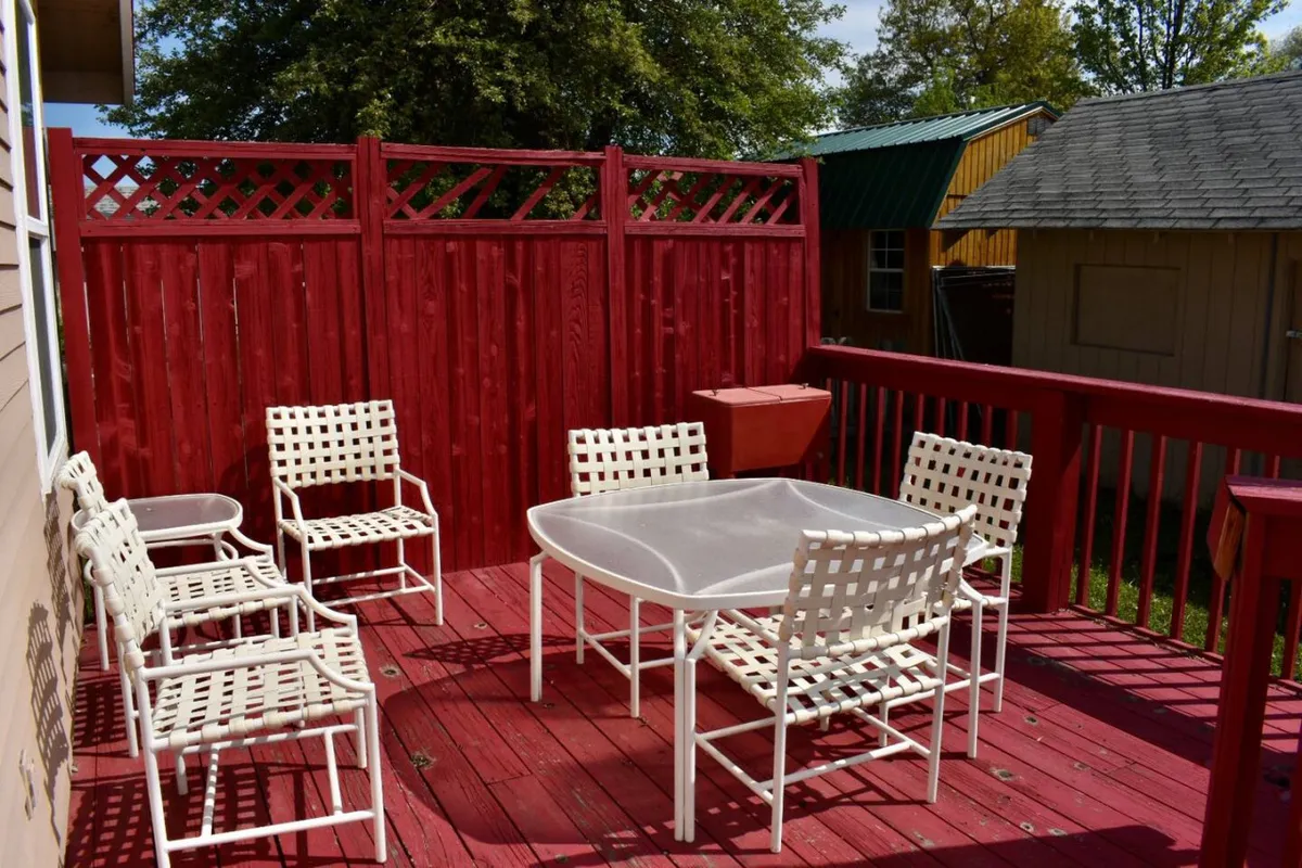 A cheerful outdoor dining area featuring white patio furniture arranged on a deck, enclosed by a red wooden fence. The setup encourages al fresco dining and social gatherings under the open sky.