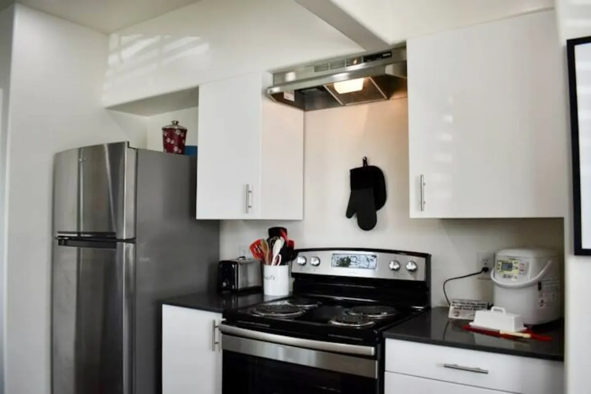 A spacious kitchen featuring a stainless steel refrigerator, black stove, white cabinets, and a range of cooking utensils organized on the counter. The space is designed for easy meal prep and social cooking.