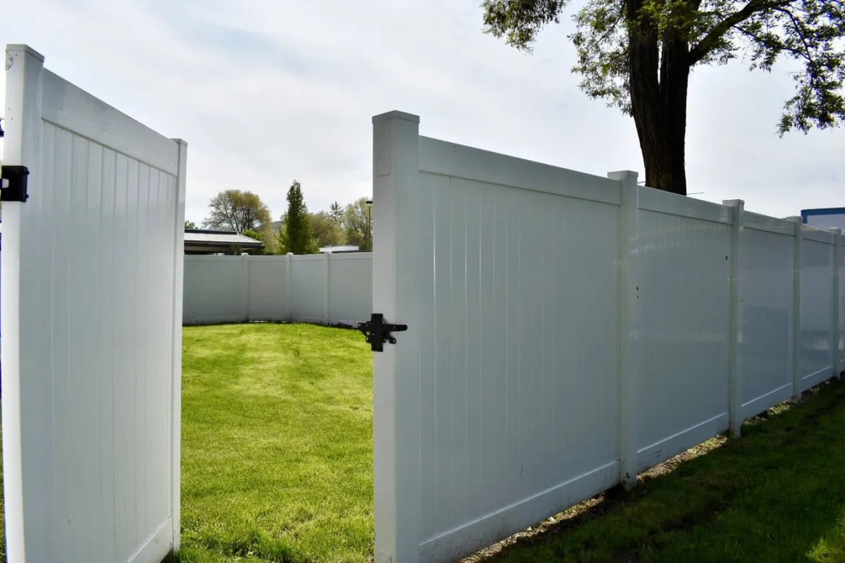 A lush green yard with a white fence and an open gate, ready for children or pets to play. The space is inviting for both gatherings and casual outdoor activities.
