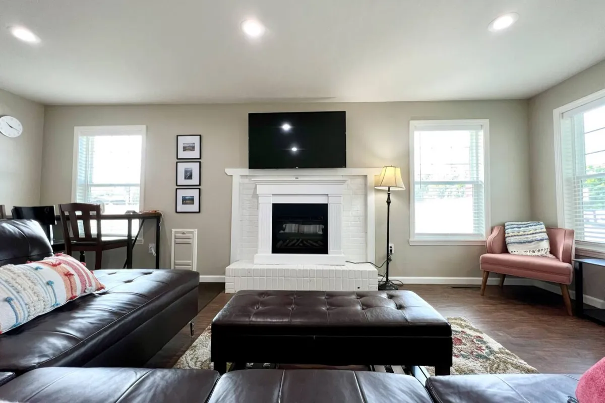 A cozy living area with a fireplace, television, sofa, armchair, and dining table. The sofa likely doubles as a queen hide-a-bed, offering flexible sleeping space for larger groups. The overall mood is warm and welcoming.