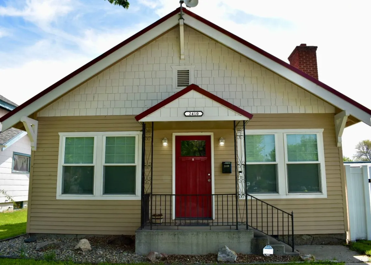 A welcoming exterior view of Quinn's Cottage featuring a red front door, white window frames, and a cozy porch—inviting guests to experience the comfort of this downtown home before heading out on their adventures.